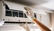 © Netsai - A person in white gloves is servicing a wall-mounted air conditioning unit, inspecting its internal components.