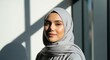 © SteffCunha - A woman wearing a grey hijab standing in front of a window with shadows on the wall.