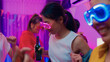 © tirachard - Closeup group multiethnic young adult Asia friend wear futuristic neon glowing glasses dance and drink alcohol beer fun hangout party in living room night indoor home. Disco lights illuminating house.
