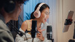 © tirachard - Close-up Young happy Asia couple wear headphone sit on desk online live streaming football live score watch soccer sport game on laptop use microphone talk with follower small studio in home at night.