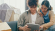 © tirachard - Young happy Asia couple sit on sofa couch use digital tablet online shopping furniture from decoration store in living room at home. Husband wife move new house, Apartment Rent And Ownership Concept.