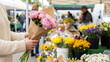 © CK Studio - Woman holding a beautiful pink peony bouquet at a vibrant outdoor farmer's market, surrounded by fresh flowers.