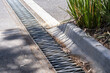 © Doublelee - Urban street curb with stormwater drainage grate and roadside gutter system beside a paved roadway. City infrastructure, stormwater management, and urban drainage for flood control and water runoff