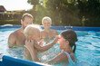 © Halfpoint - Young family with two children in swimming pool outdoors in backyard garden.