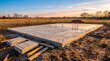 © Yudi - A freshly poured concrete slab house foundation awaiting construction, illuminated by the warm glow of sunset
