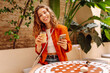 © maxbelchenko - Portrait of a smiling woman with a phone and an iced coffee on a cozy cafe terrace. A young woman sips a drink and texts in a cozy setting. Concept: drinks, blogging, and relaxation.