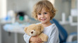 © Nataliya - Young child visiting dental clinic holding teddy bear, smiling expression bright room, daytime pediatric dental care, with copy space