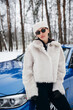 © Petro - Young woman standing outside her car in winter