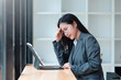 © amnaj - Young Asian businesswoman sitting with headache and stress from working on a tablet, facing burnout and pressure at office