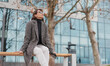 © olezzo - Attractive mature business woman in eyeglasses and coat resting on a bench near office building in spring