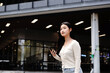 © Stella 16 - asian woman college student looking around holding smartphone walking in campus