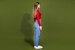 © deagreez - Young woman in red top and blue jeans stands in profile against olive green background showcasing casual fashion and lifestyle
