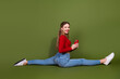 © deagreez - Young woman in red top stretches on a green studio backdrop while holding a red phone