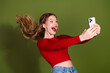 © deagreez - Young woman in red top takes a selfie with joyful expression against a green background