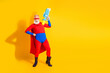 © deagreez - Energetic elderly superhero in red blue costume with cape and toy ray gun poses against yellow background for a bold fun stock photo
