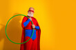 © deagreez - Senior superhero in red and blue costume with cape holds a green hoop against a bright yellow background for playful retro style and entertainment