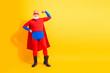 © deagreez - Senior superhero stands proudly in red and blue costume with cape and mask against a bright yellow background for stock photography use