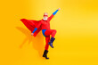 © deagreez - Red cape superhero leaps on bright yellow background during energetic performance for holiday celebration and advertising use