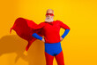 © deagreez - Elderly bearded superhero in red and blue costume poses confidently with cape on yellow background showing bold stage presence