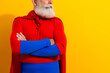 © deagreez - Bearded senior superhero in red cape and blue suit poses confidently against bright yellow background