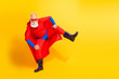 © deagreez - Senior superhero in red cape kicks with energy against bright yellow background for a fun dynamic promotional image