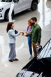 © djile - Dealer handing car keys to happy couple buying new car