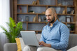 © Liubomir - Young man telecommuting on a laptop from his comfortable living room sofa, focusing on work tasks and embracing flexible remote office employment at home