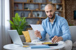 © Liubomir - Adult man reviewing documents, using a calculator and laptop, managing his personal finances and bills from a modern home office setting to stay organized with his budget
