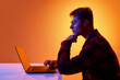 © master1305 - Side view of man analyzing information on laptop in modern neon studio setting. Concept of data review process, strategic planning and focused business research.