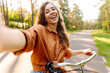 © maxbelchenko - A happy woman with a phone and a bicycle in a sunny park. A beautiful woman rides a bicycle, blogs, and enjoys the sunset. Blogging, weekend concept.