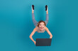 © deagreez - Young woman jumping with laptop on a bright blue background ready for online shopping and modern lifestyle advertising
