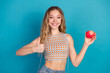 © deagreez - Young woman with apple and thumbs up against blue background stock photo
