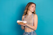 © deagreez - Young woman with measuring tape holding plate of cookies against blue background in casual fashion