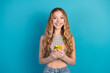 © deagreez - Young woman with blond hair smiles while holding a yellow phone against a blue background