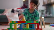 © Marco - Young boy building with colorful wooden blocks, concentrating on assembling a structure, exploring creativity and imagination during indoor play in a cozy living room