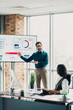 © deagreez - Presenter explains data on a large screen to colleagues in a bright loft office during a collaborative business meeting