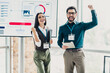 © deagreez - Two business professionals celebrate success during presentation in a modern loft office with a digital chart display