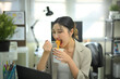 © Prathankarnpap - Businesswoman eating instant noodles at office desk, casual lunch break during workday in modern workspace.