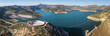 © AmazingAerialAgency - Aerial view of a vibrant blue lake reflecting the clear sky, surrounded by rugged mountains and a unique circular structure, Lakeside, California, United States.