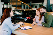 © djile - Couple discussing car purchase with saleswoman at dealership desk