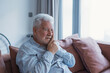 © Daniel - A senior man rests on the couch at home touching his jaw with a pained expression, reflecting dental pain and health concerns that disrupt his comfort and daily routine