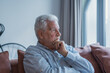 © Daniel - Sad elderly man sits alone on a sofa at home, looking out the window with a worried expression. He reflects on challenges and feels stressed, illustrating loneliness and concern.