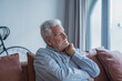 © Daniel - An older man gazes through the window from his couch with a troubled face, feeling isolated and anxious as he contemplates personal concerns and uncertainty in his daily life