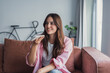 © Daniel - A happy young woman relaxes on a comfortable sofa at home, sending an audio message and sharing news with friends while enjoying a peaceful weekend and using voice assistant technology