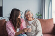 © Daniel - Smiling older mother and adult daughter using phone together, sitting on cozy sofa at home, happy young woman and mature mum looking at smartphone screen, watching video, having fun, two generations