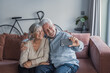 © Daniel - An elderly husband and wife pose for a photo with a smartphone, laughing and embracing as they enjoy a fun and playful moment while recording a video at home