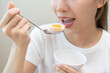 © KMPZZZ - Protein in food, happy smiling asian young woman, girl in diet holding boiled egg, eat with spoon for breakfast in the morning at home. Health care, loss weight people concept, isolated on background.