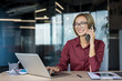 © Liubomir - Young businesswoman smiling while talking on her smartphone and typing on a laptop at a modern office desk, confidently multitasking and staying productive during remote work