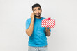 © khosrork - Portrait of satisfied delighted smiling unshaven man wearing blue T- shirt standing with gift box in hands, talking phone, boasting his present. Indoor studio shot isolated on gray background.