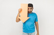 © khosrork - Sad upset stressed unshaven man wearing blue T- shirt standing showing paper arrow indicating down, looking at camera with disappointed expression. Indoor studio shot isolated on gray background.
